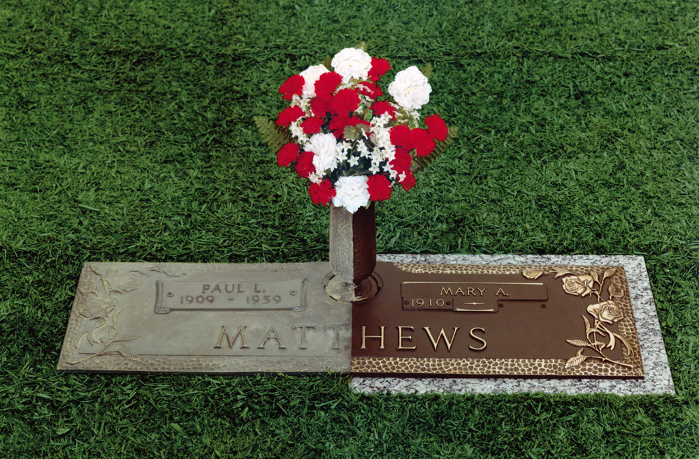 restored grave maker with red and white flowers