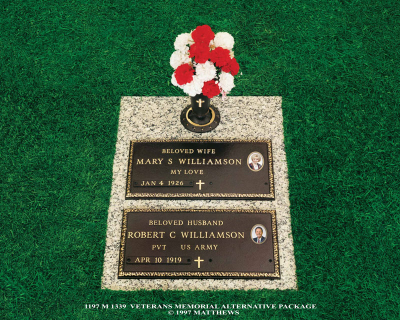 stone grave marker with two bronze plaques and red and white flowers